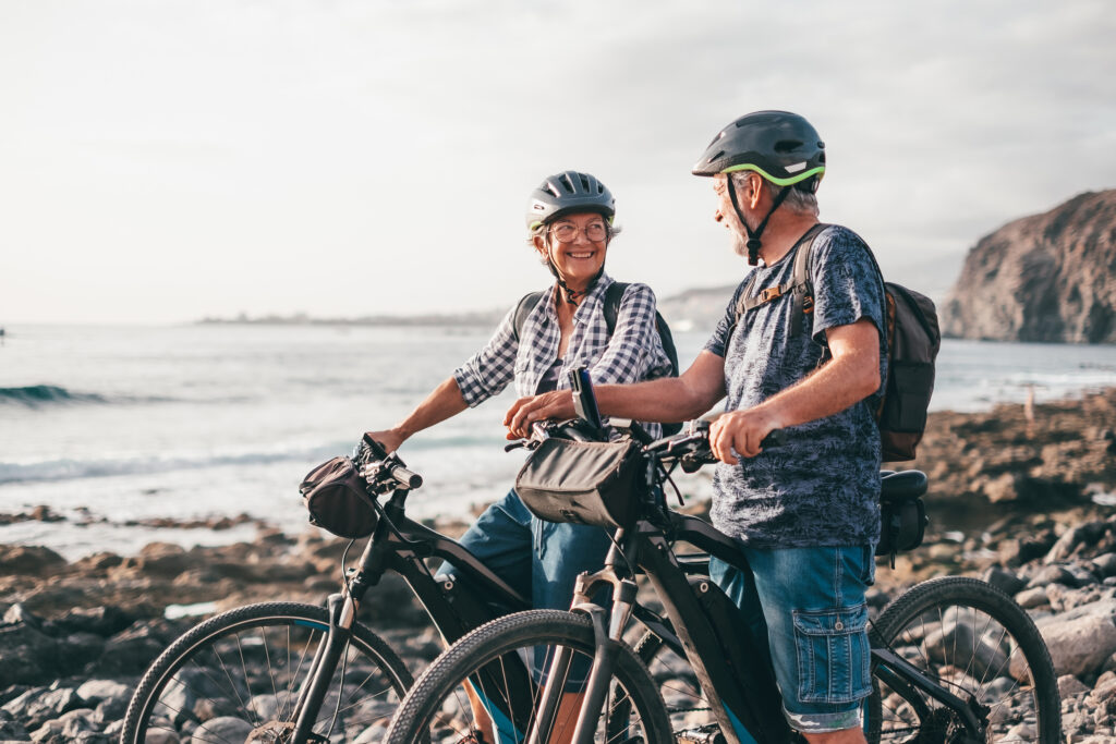Happy couple of athletic seniors with their bicycles at the beach. Elderly people expressing satistaction and freedom in vacation or retirement